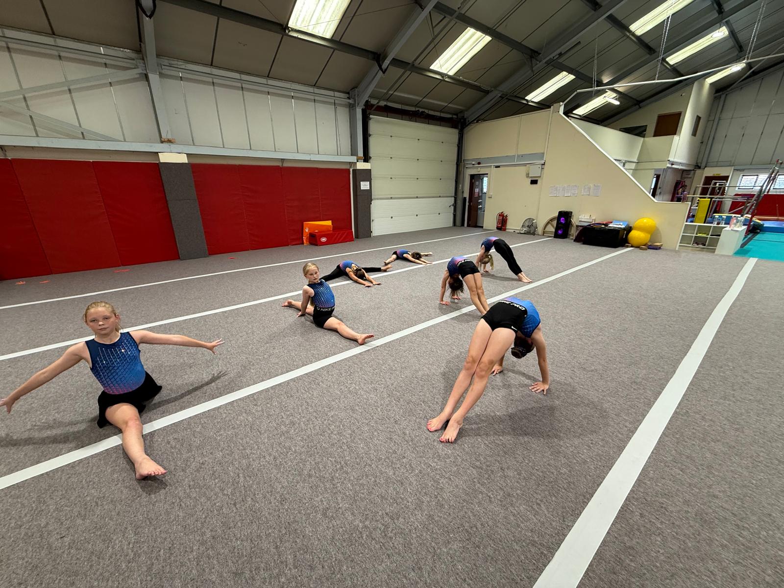 Girls squad gymnasts stretching and practising bridges on the floor at Maldon Gymnastics Club